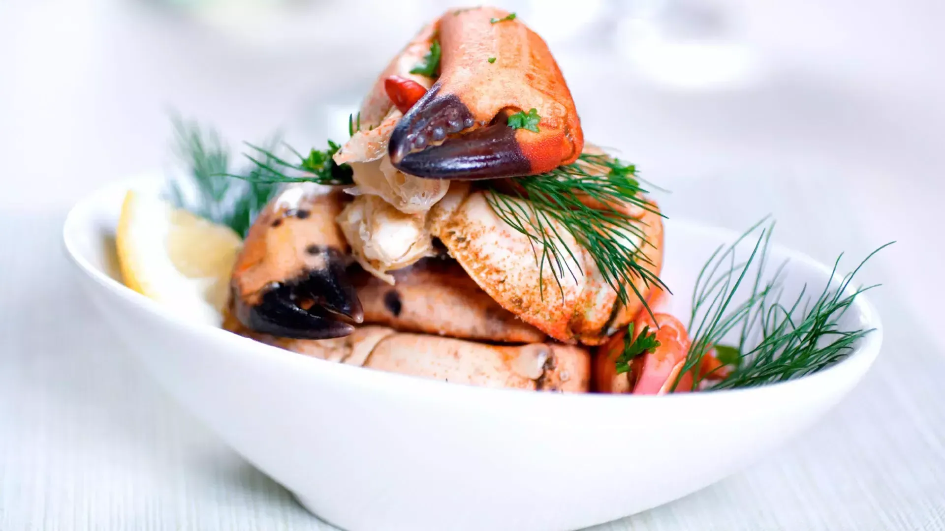 Crab legs are stacked in a white bowl and sprinkled with fresh dill.